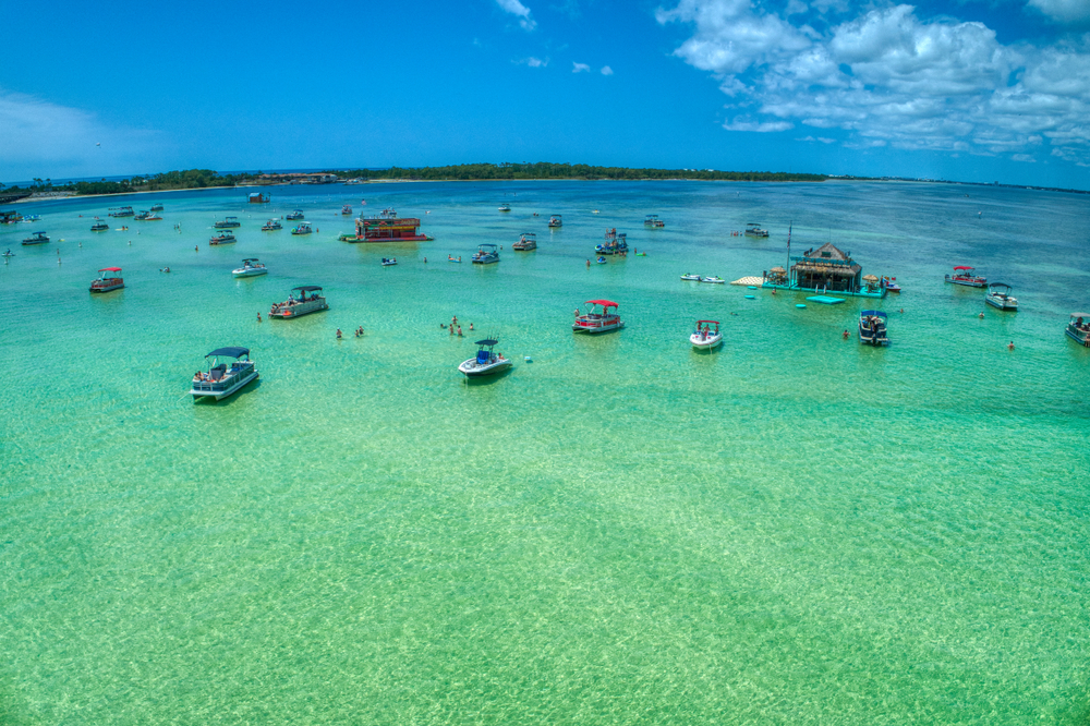 A bunch of boats on Crab Island, one of the coolest islands in the south. It is a sandbar, so the boats are floating and there are people swimming and standing on the sand bar. 