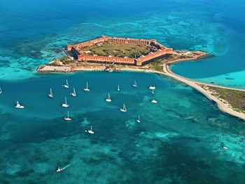 An aerial view of Dry Tortugas National Park, one of the best islands in the south. You can see a large fort, crystal blue water, and sail boats in the ocean.