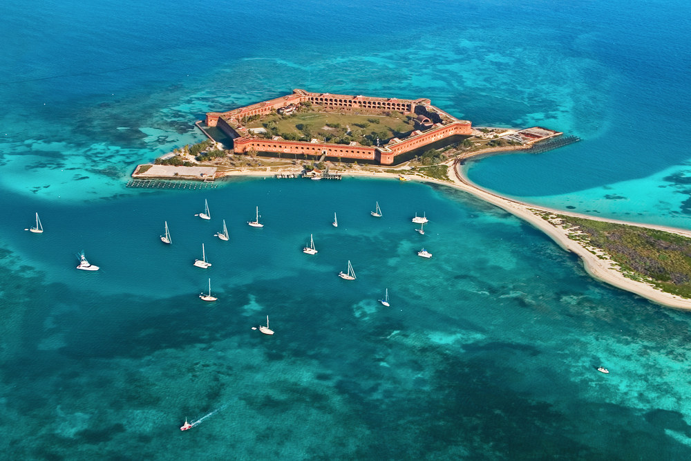 An aerial view of Dry Tortugas National Park, one of the best islands in the south. You can see a large fort, crystal blue water, and sail boats in the ocean.