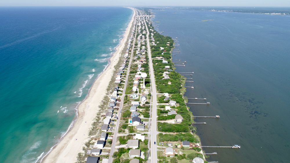 An aerial view of Emerald Isle, a long skinny island outside of North Carolina. On one side you can see the shore and on the other there are individual decks for the beach houses. 