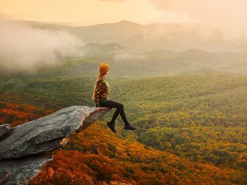 girl sitting on edge of large rock overlooking autumn valley while hiking in Boone