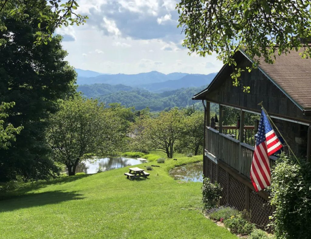 The side of a cabin with views of the landscape. You can see two small ponds, lots of trees, and large mountains in the distance. One of the best cabins in Boone. 
