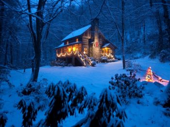 A log cabin in the woods at night in the winter. There is snow on the ground and the cabin has string lights on it. One of the best cabins in Boone.