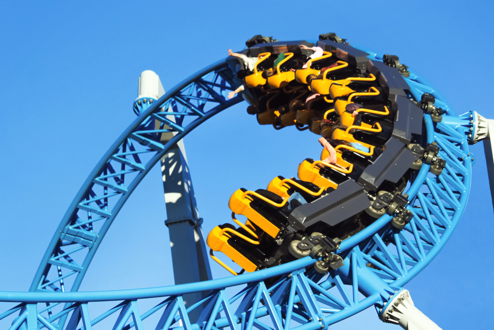 A blue rollercoaster with yellow and black seats looping in the sky. 