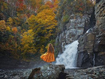 woman in orange dress standing in front of linville falls in north carolina