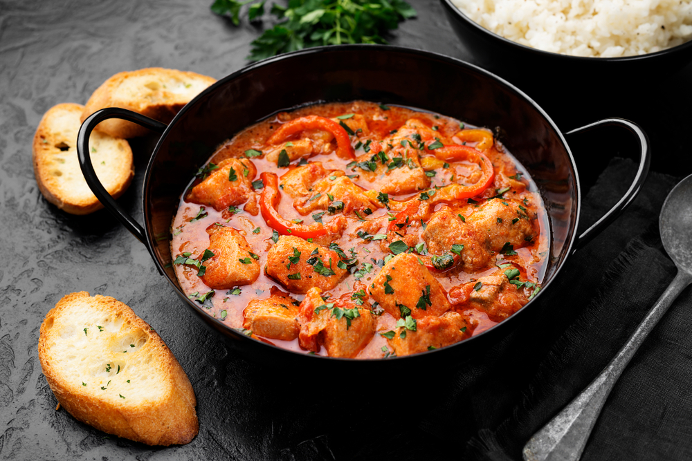 A pot of fish stew with a red sauce on a table with bread.