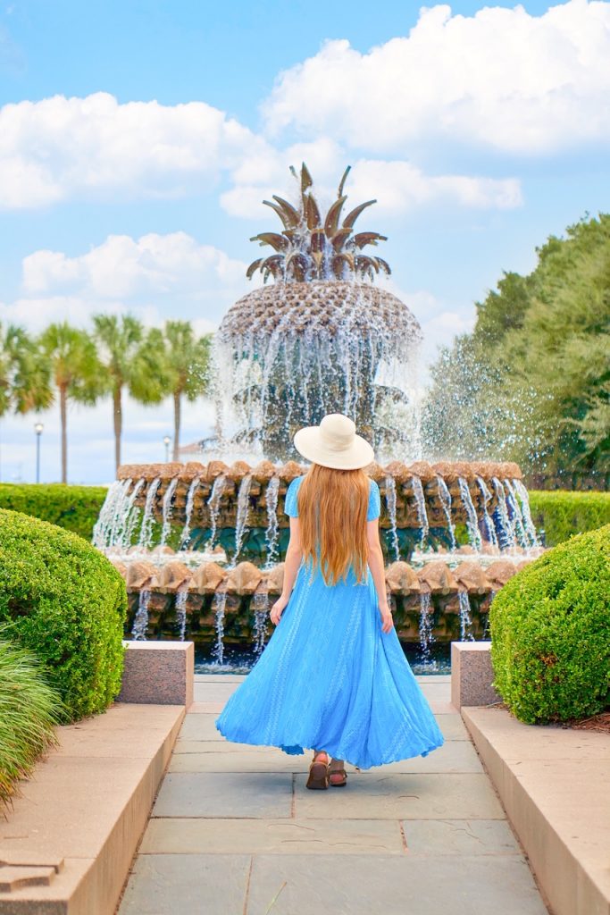 Girl in a blue dress standing in front of the Pineapple Fountain, one of the most famous things to do in Charleston.