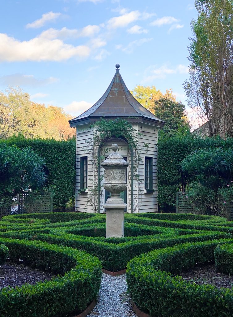 Looking into Shamrock Garden with its neat hedges, sculpture, and shed.