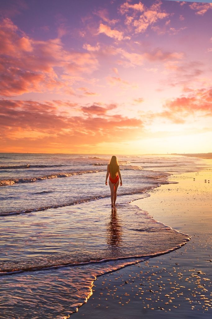 A girl in a red swimsuit walking at sunset along the beach on Sullivan's Island, one of the best places to visit in Charleston.