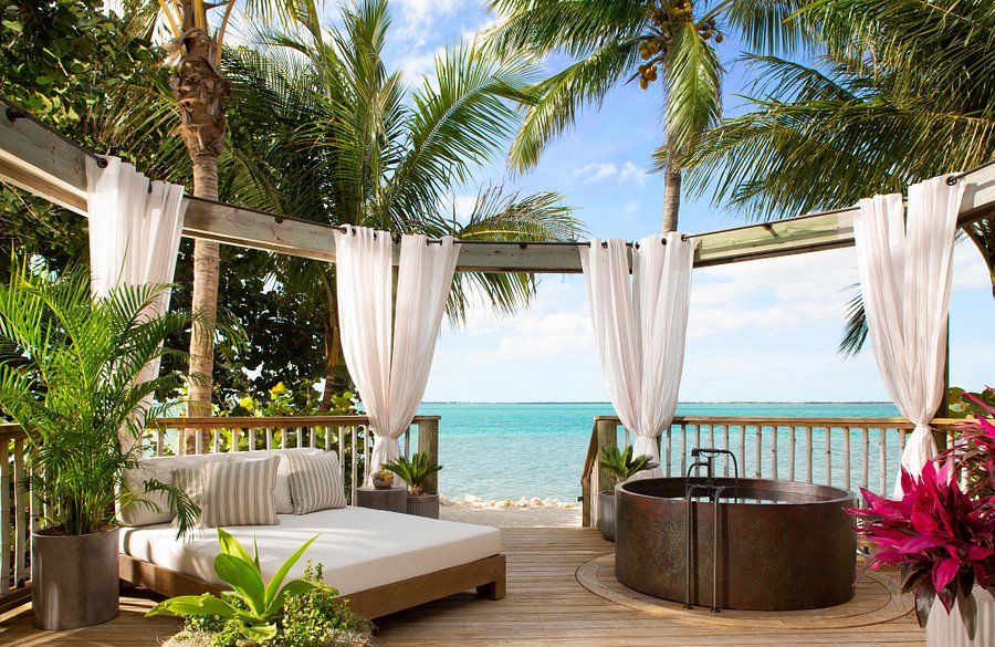 The turquoise waters surrounded by palm trees with a large soaking tub and lounge chairs
