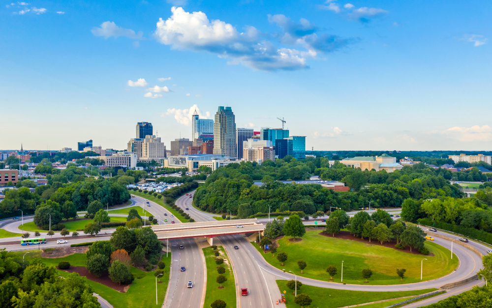 arial photo of raleigh during the day. roads overlapping one another in front of skyline