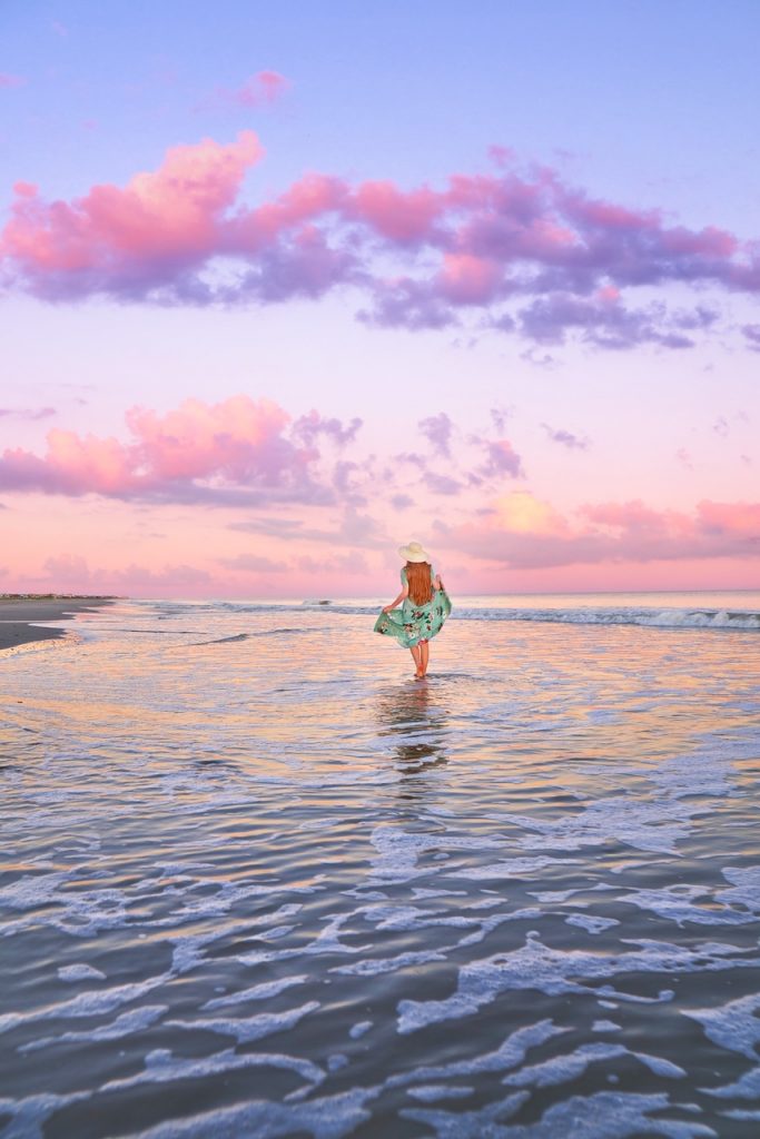 woman in floral dress on beach with blue and pink pastel sunset