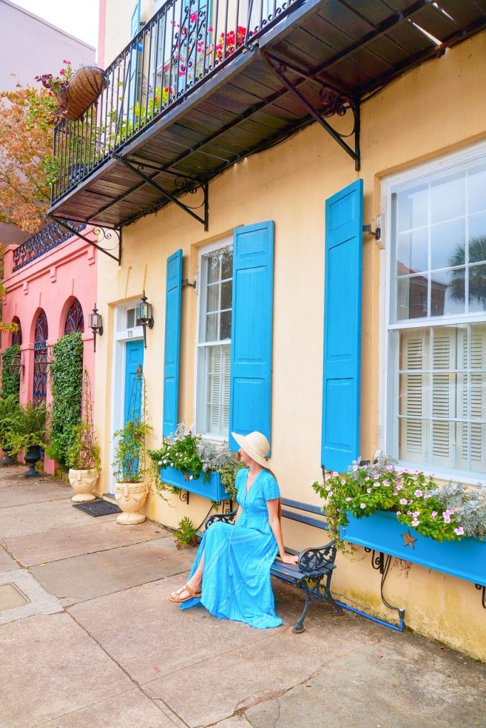 woman in blue dress sitting on bench in front of rainbow colored houses best places to visit in south carolina