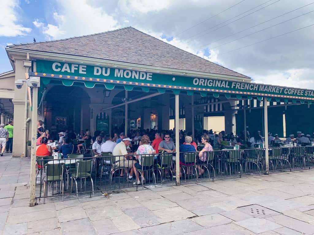 The exterior of Cafe Du Monde where you can see people sitting at tables under an awning.