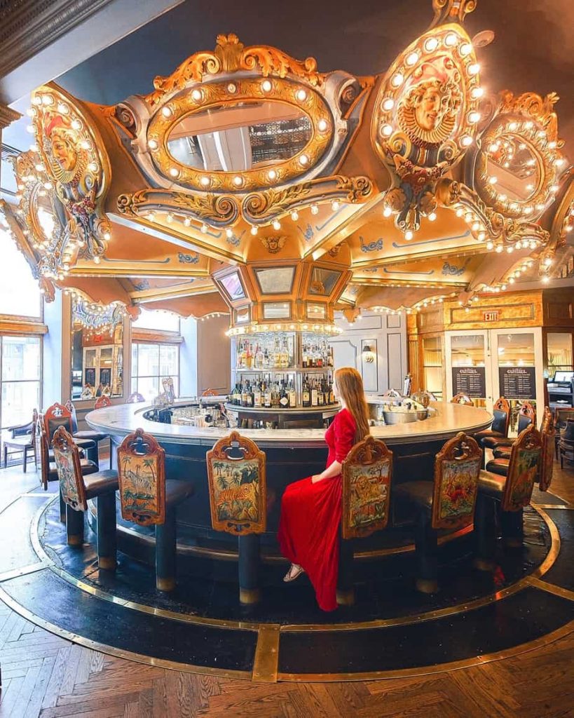 A woman in a red dress sitting at a bar in a building that looks like an old-fashioned carousel. It is all lit up.