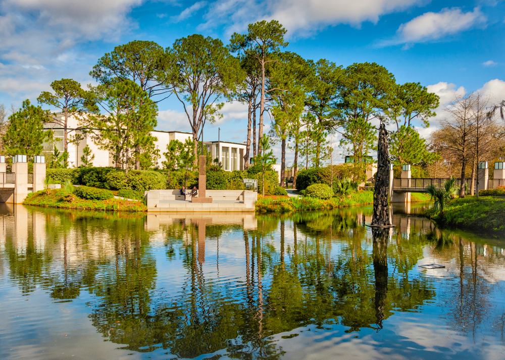 A pond in a sculpture garden on the campus of the New Orleans Museum of Art, one of the best places to visit in New Orleans. There are sculptures, trees, and buildings around the pond. 