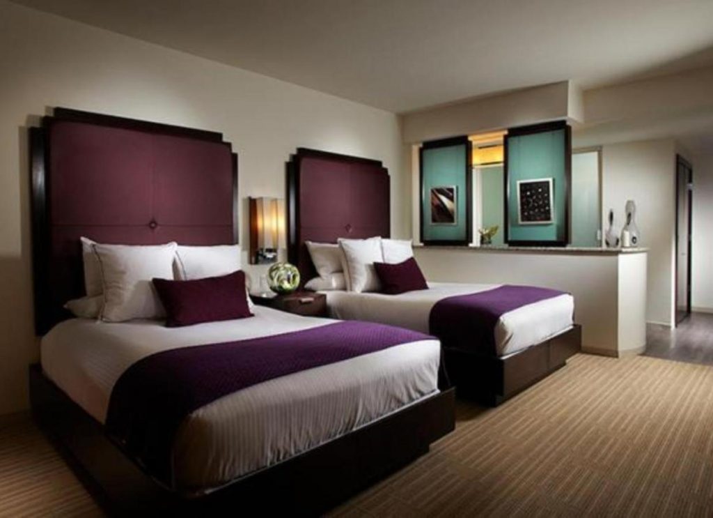 inside of a hotel room with two beds with purple decor 
