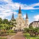 The front of the St. Louis Cathedral, one of the most popular and best places to visit in New Orleans. You can see palm trees and a walkway as well.