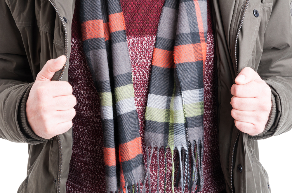 A man's hands grips his jackets and sweater and scarf to stay warm during winter in the south.