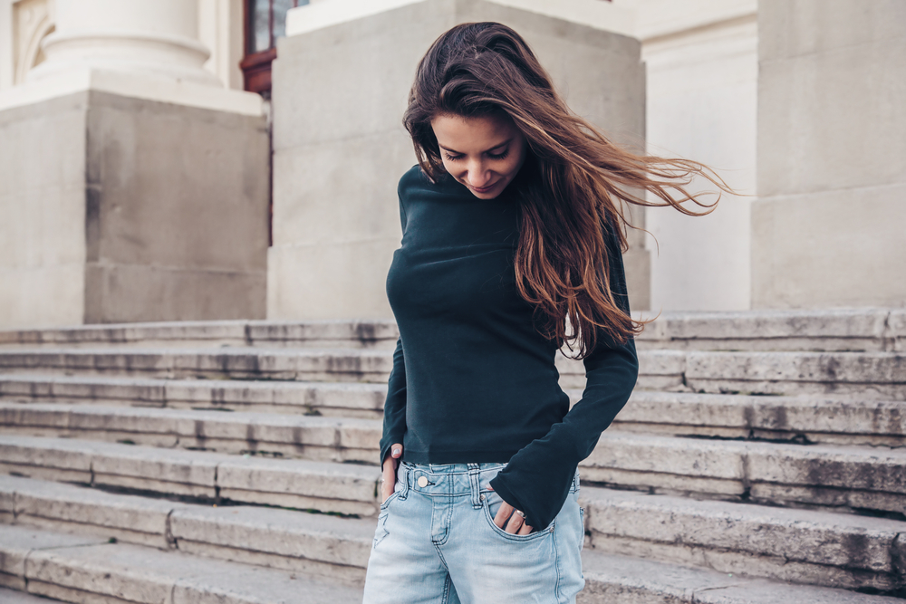 A woman looks down at her cute, green, long sleeved t-shirt, knowing she looks cute during winter in the south. 