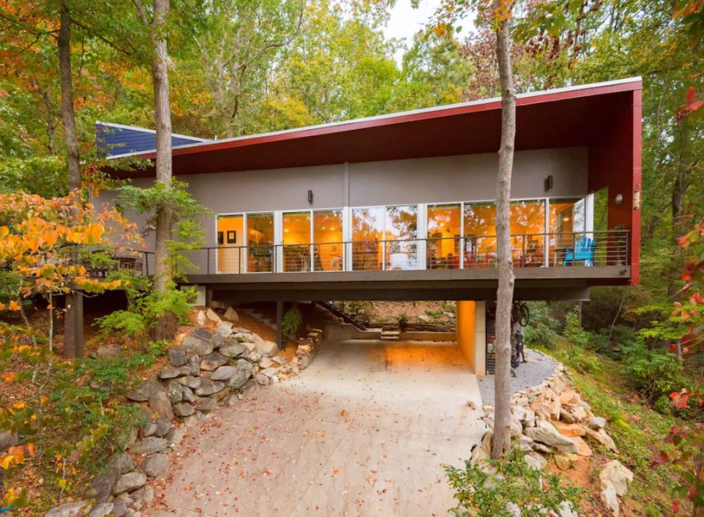 The exterior of a Mid-Century Modern style treehouse. It has a row of large windows, a front deck, and a carport. It is very angular and one of the best treehouses in North Carolina. 