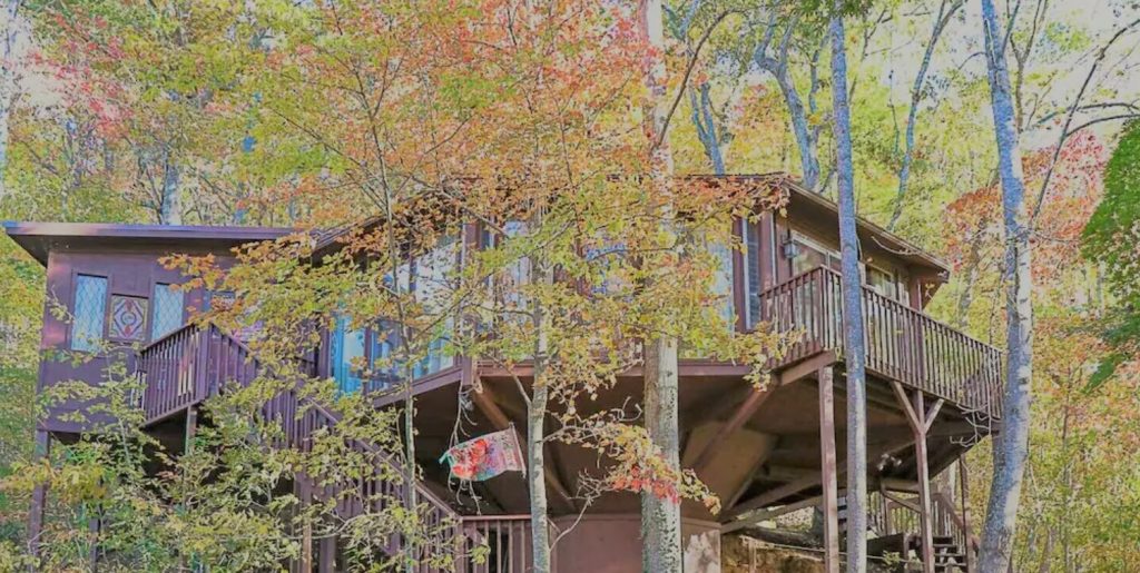 A circular treehouse surrounded by trees in the fall. You can see several decks and levels on the treehouse. 