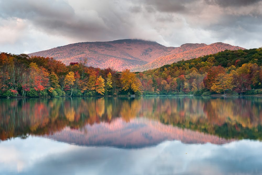 by far one of the best lakes in north carolina. calm lake water with fall colored trees and mountains behind the water