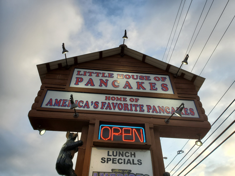 The cabin-shaped wooden sign for "Little House of Pancakes" with the neon "Open" sign illuminated, one of the best places for pancakes in Gatlinburg.