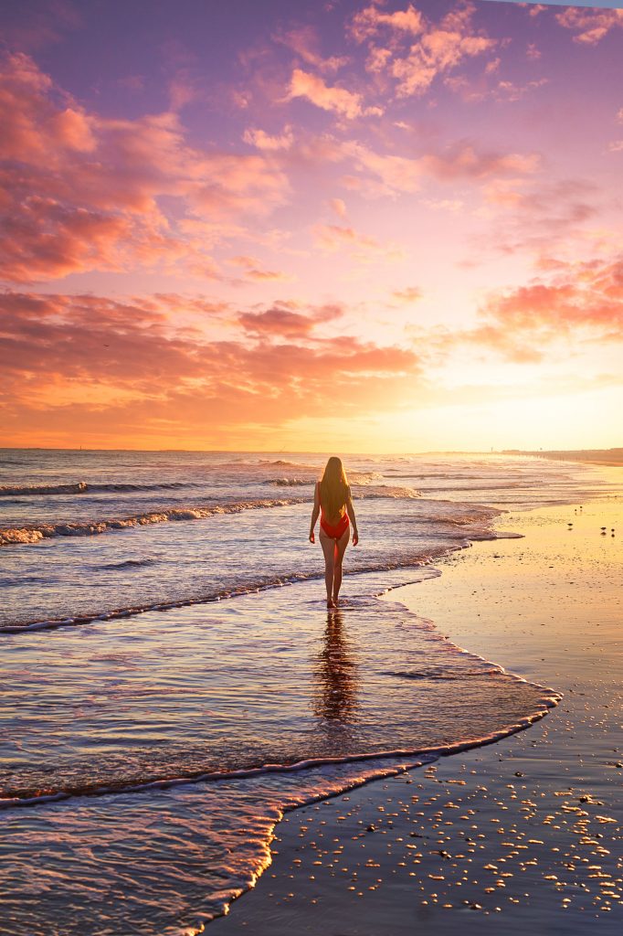 Woman in red swimsuit walking along the beach with a gorgeous sunset!