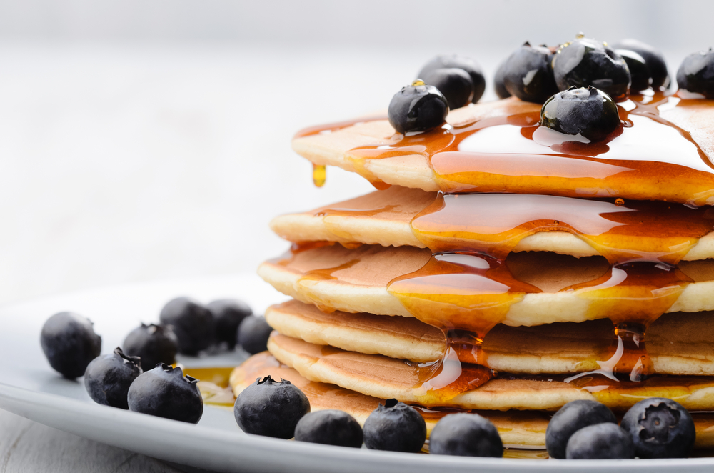 Close-up of a stack of pancakes covered in syrup and blueberries.