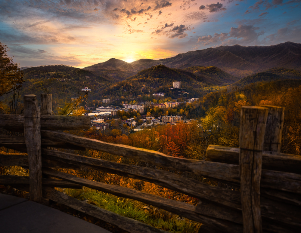 Gatlinburg nestled in the mountains at sunset with a wooden fence in the foreground.