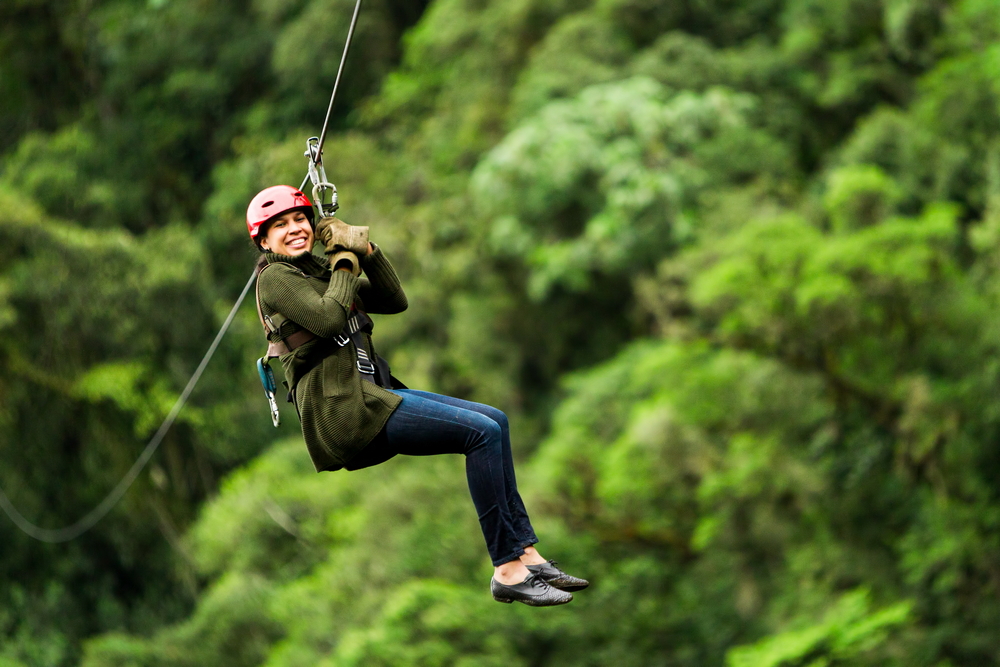 Woman going down a zipline with trees in the background.