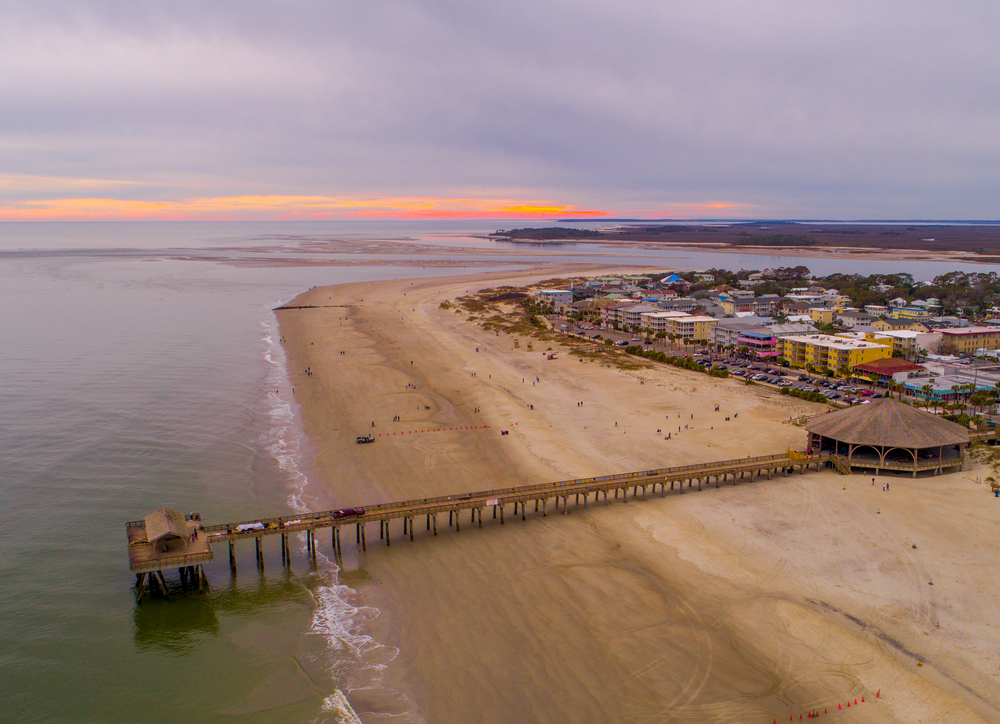 Aerial view of Tybee beach featuring a pavillion and pier and buildings in the background. 