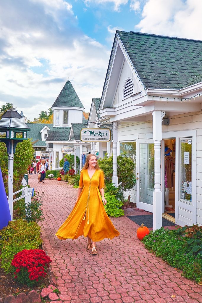 A woman in a yellow dress walking down a brick path. There are white buildings that have shops on them along the brick path. 