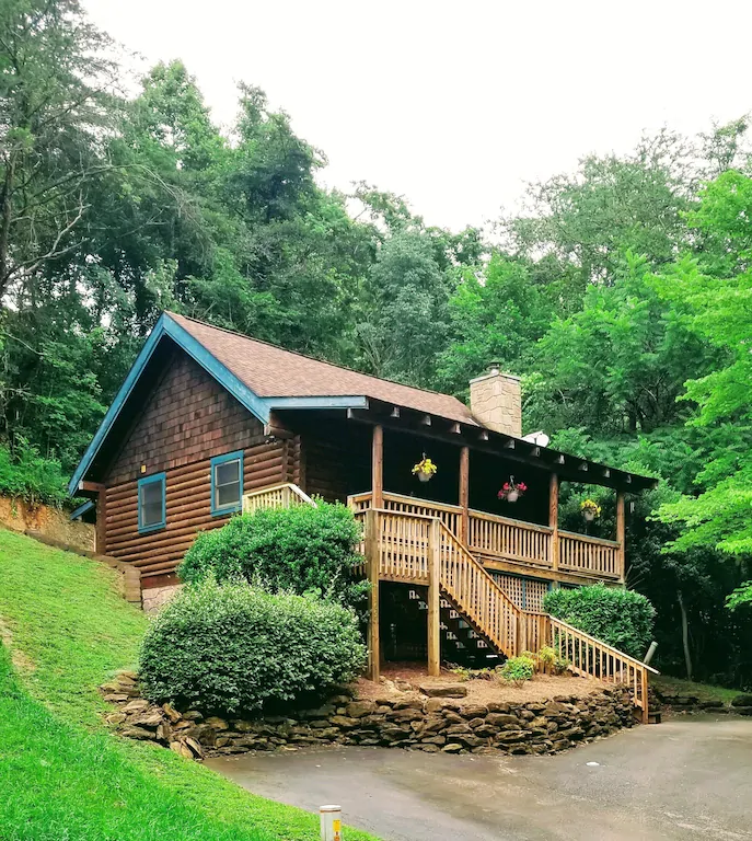 A two story log cabin with trees behind it. One of the cabins in Tennessee to stay in.   