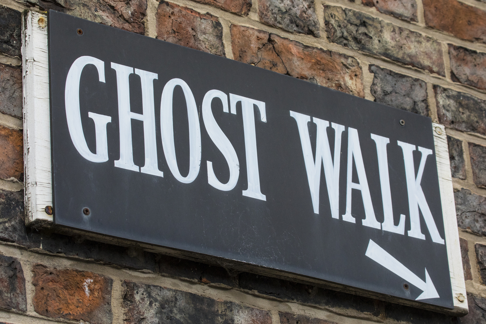 A black sign that says 'Ghost Walk' in white with an arrow pointing to the right. It is mounted on a brick wall. 