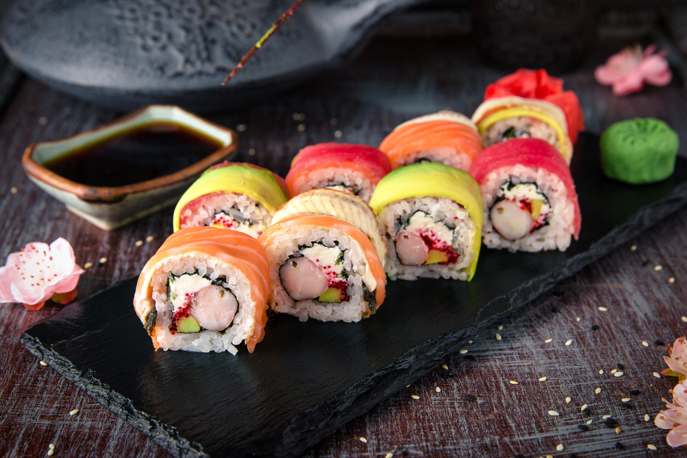 Sushi on a plate slate with a side of soy sauce. 