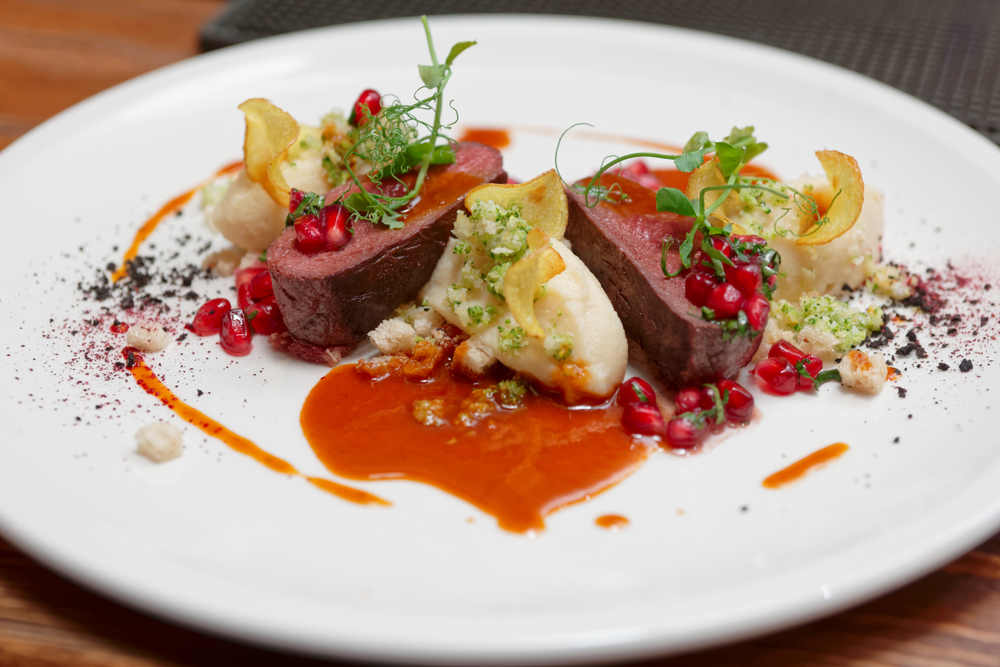 Venison on a white plate with a pomegranate sauce. In an article about restaurants in Nashville. 