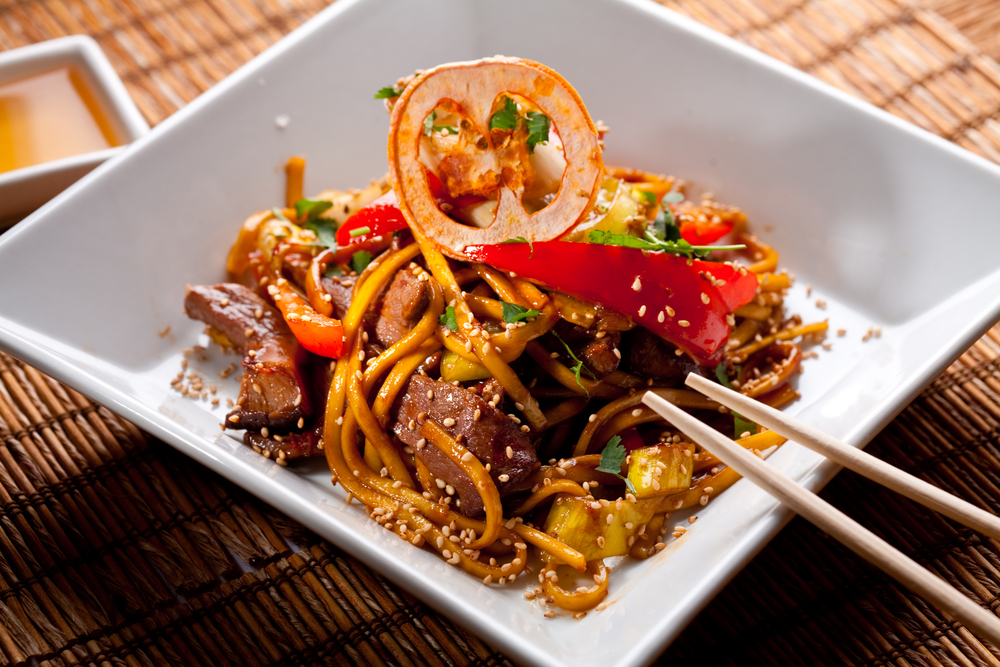 Noddles and meat and peppers on a bowl with chop sticks  