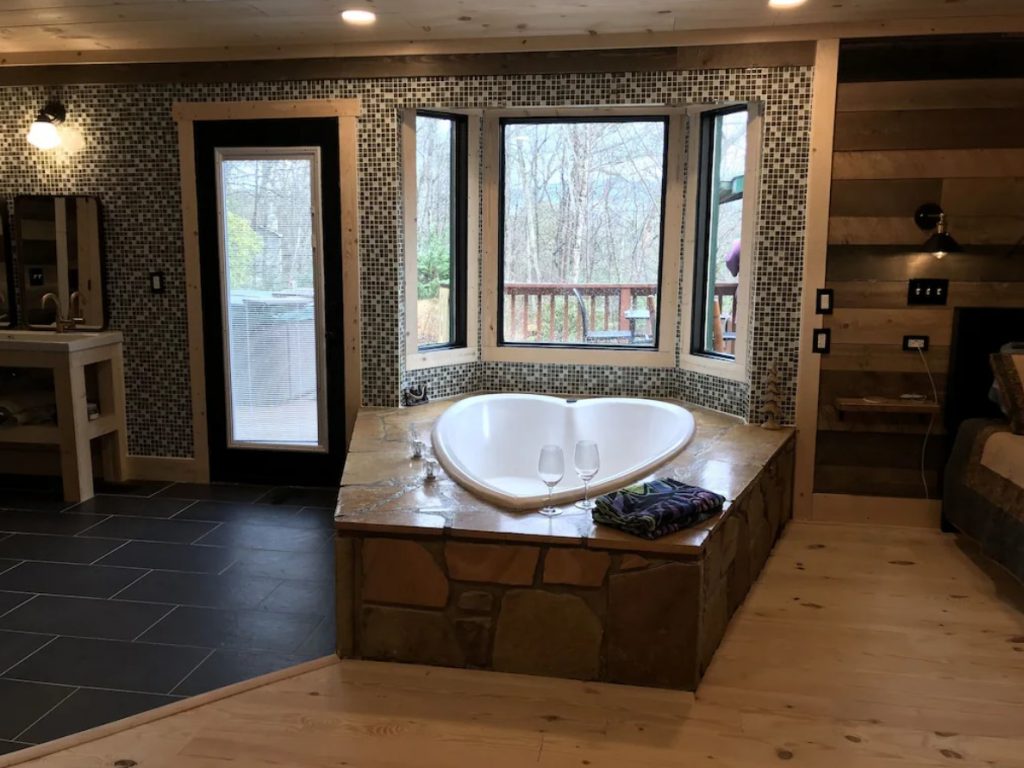 A white heart shaped jacuzzi tub in a luxurious bathroom that overlooks a wooded view. It's one of the best cabins in Gatlinburg. 
