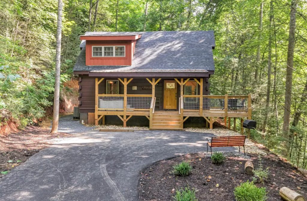 The front of a modern cabin with a large wrap around porch and a stone driveway in the front. Its surrounded by woods. It's one of the best cabins in Gatlinburg Tennessee. 