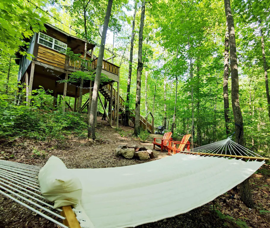 View of a teeehouse from below with a hammock and firepit in the foreground. 