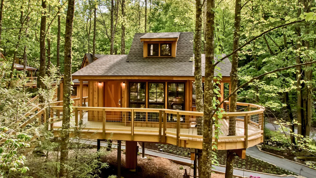 A treehouse among the trees with large windows and a dormer window to enjoy the view. 