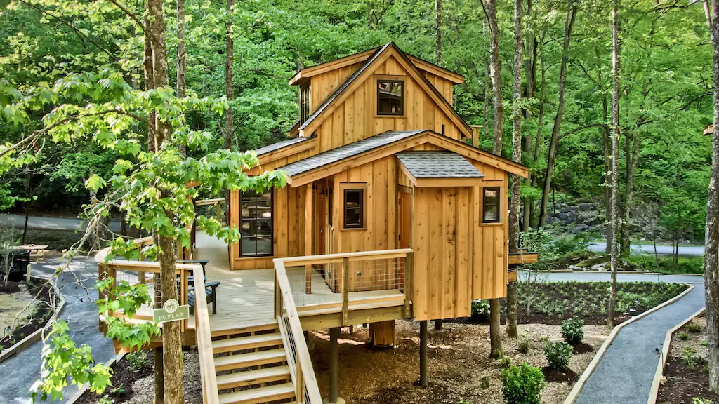 A raised cabin with a deck surrounded by a manicured garden and paths. 