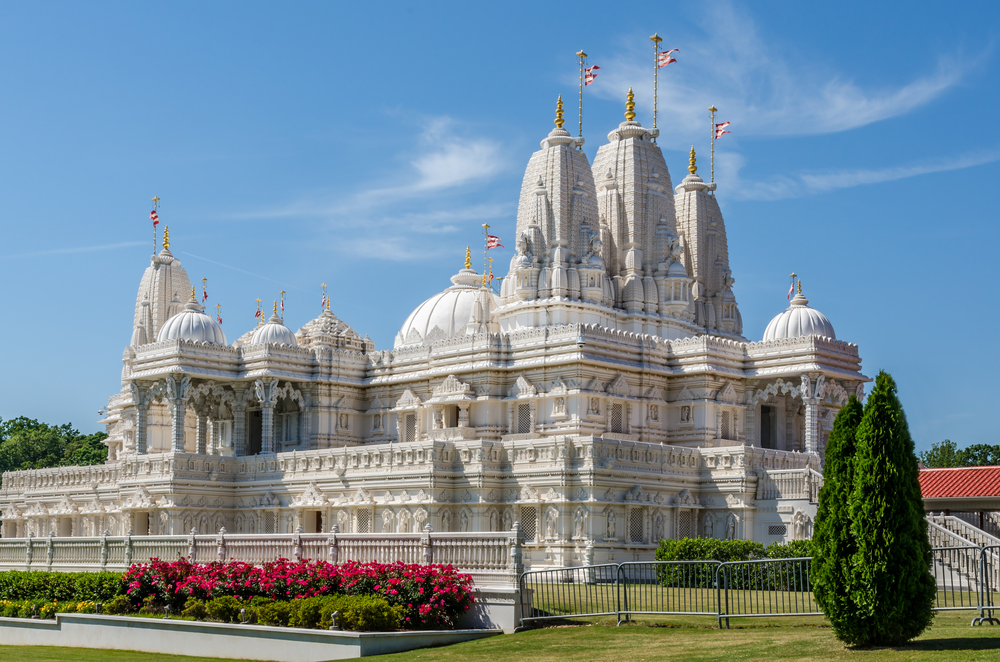 A large white Hindu Temple that is ornately carved. It is sitting on a green lawn and has flags on top of it. It's one of the best hidden gems in Georgia. 