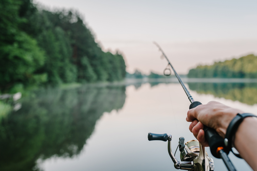 A man's hand casts a fishing rod. We are looking from his perspective out onto the water. Cheatham Lake is known for its fishing scene.