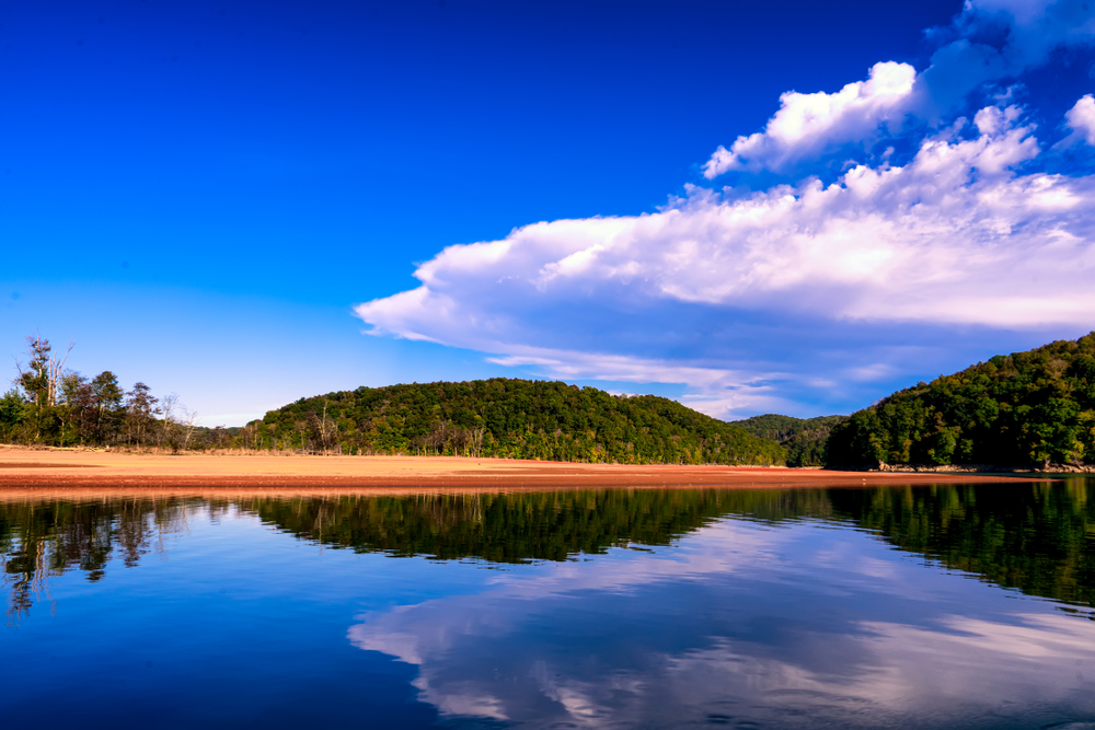 This wide shot of Norris Lake shows why it is one of the best beaches in Tennessee: sandy beaches stretch for miles along the shoreline, providing plenty of room for various activities. Part of Norris Lake's beaches are pictured here with thick green forests resting in the background and reflected in the glassy surface of the lake.