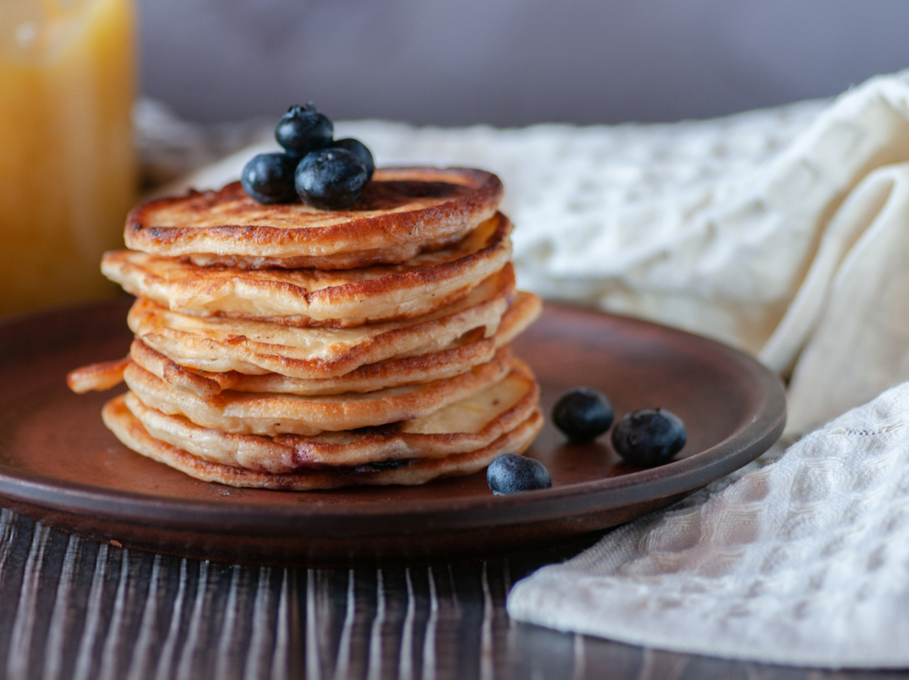 A stack of pancakes topped with blueberries sits on a ceramic plate, with white linen napkins in the background. Pancake are very popular for breakfast in Pigeon Forge. 