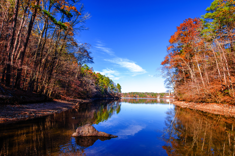 Clear blue water with trees on either side, showcasing the beautiful fall colours in Arkansas state parks. 