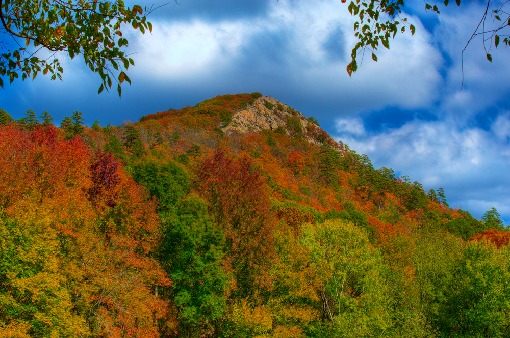 Pinnacle mountain covered in beautiful red, orange yellow and green fall foliage and a blue sky, showing one of the most beautiful state parks in Arkansas. 